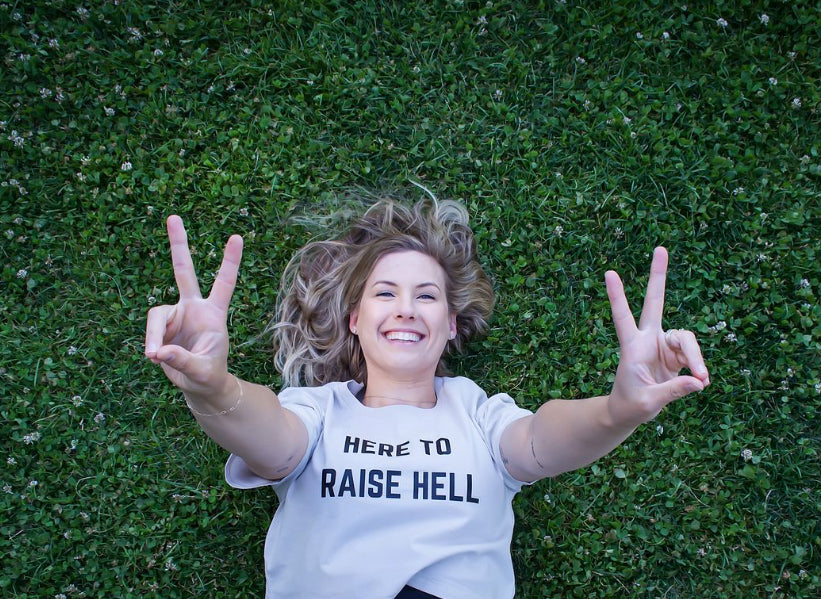 Girl wearing here to raise hell crop tshirt while holding peace signs